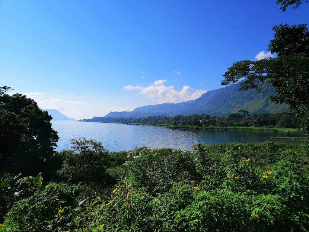 [Sunlight breaks through the clouds over Lake Toba, highlighting its natural beauty as detailed in this Indonesia travel guide.]