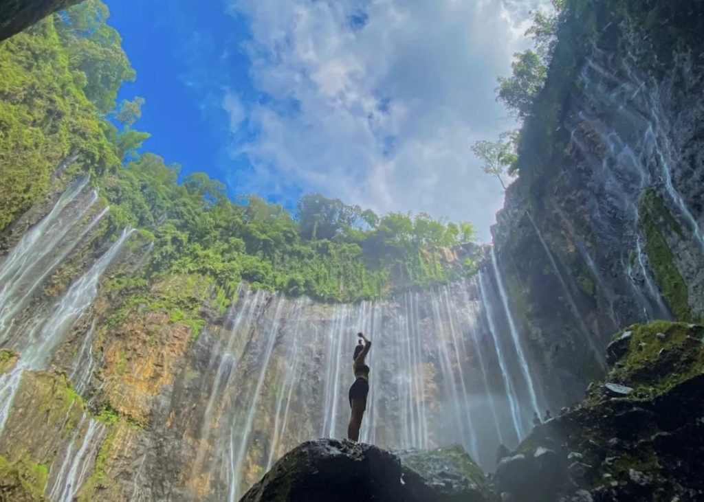 [A visitor gazes at the immense Tumpak Sewu Waterfall, a truly breathtaking sight and one of the most adventurous things to do in Indonesia.]