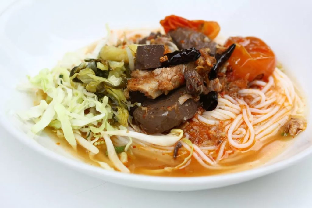 A vibrant bowl of Khanom Jeen Nam Ngiao with rice noodles, pork, and tomatoes.
