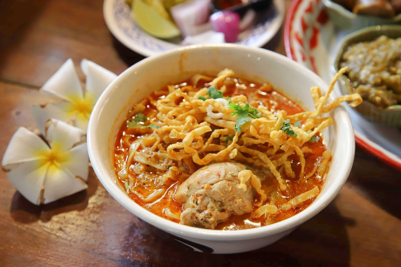 A rich and creamy bowl of Khao Soi noodles topped with crispy noodles and fresh herbs.