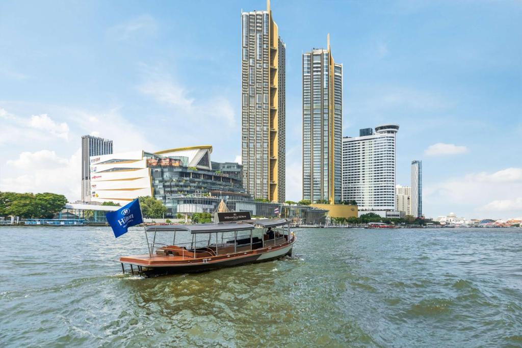 A modern guest room at the Millennium Hilton Bangkok with a stunning view of the city skyline and Chao Phraya River at twilight.