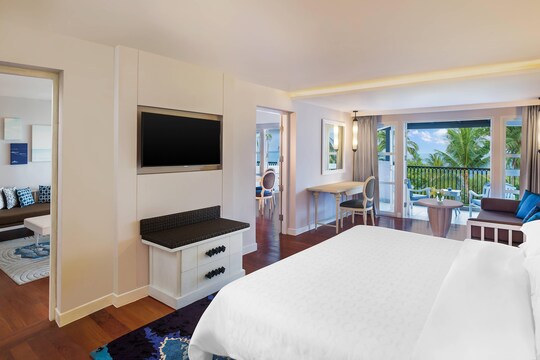 A spacious and modern suite at the Sheraton Samui Resort, with a comfortable bed and a balcony overlooking the resort's lush gardens.