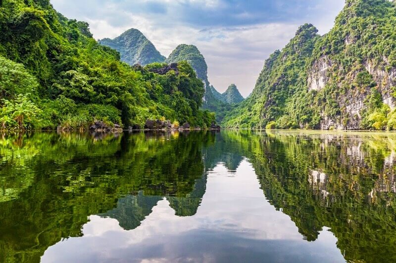 [The serene reflection of karsts and lush greenery on the calm river waters of Ninh Binh.]
