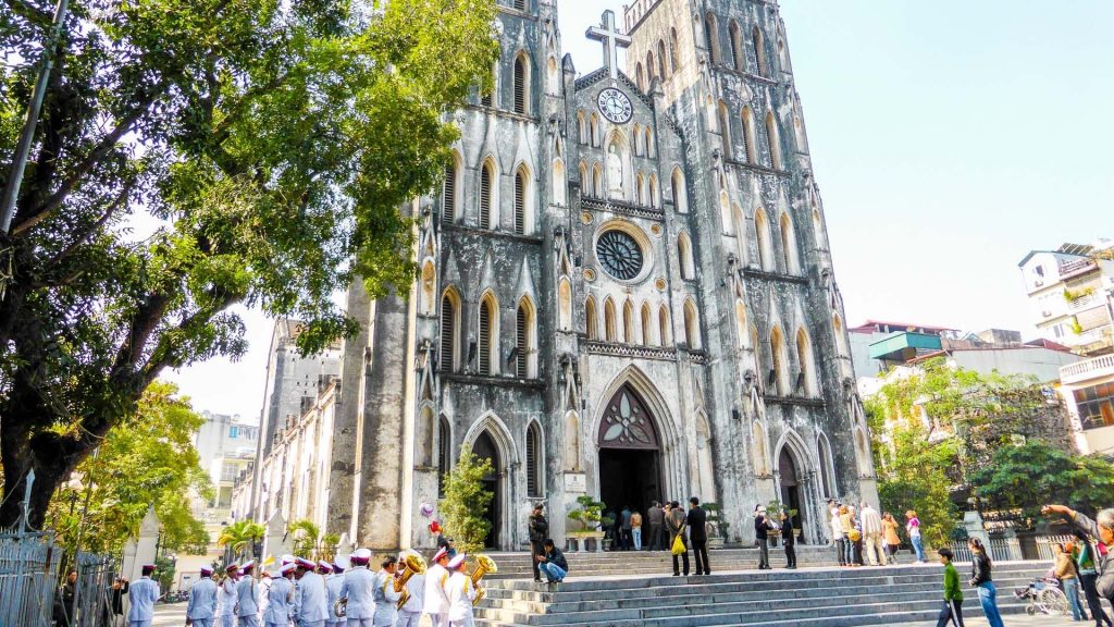 [The impressive neo-Gothic facade of St. Joseph Cathedral in Hanoi, with a group of people in white ao dais in front.]