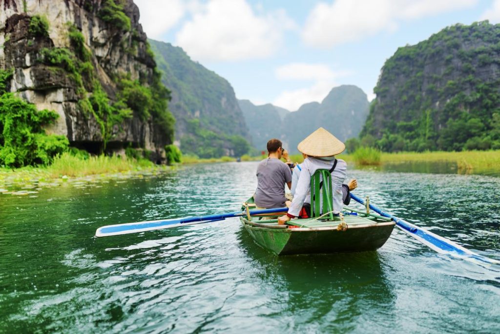[A tranquil scene of a local woman rowing a sampan boat along a river in Ninh Binh, one of the most peaceful things to do in Vietnam.]